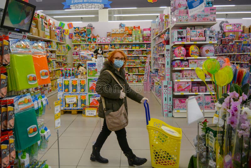Starsza kobieta w sklepie z zabawkami, żółty koszyk. dama z maską do twarzy spaceruje po korytarzu w supermarkecie fotografia stock
