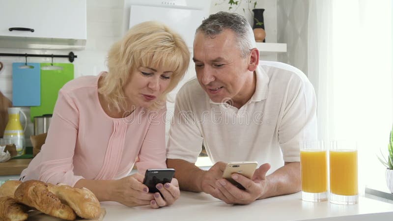 Starsza rodzinna para cieszy się technologię cyfrową podczas śniadania w kuchni