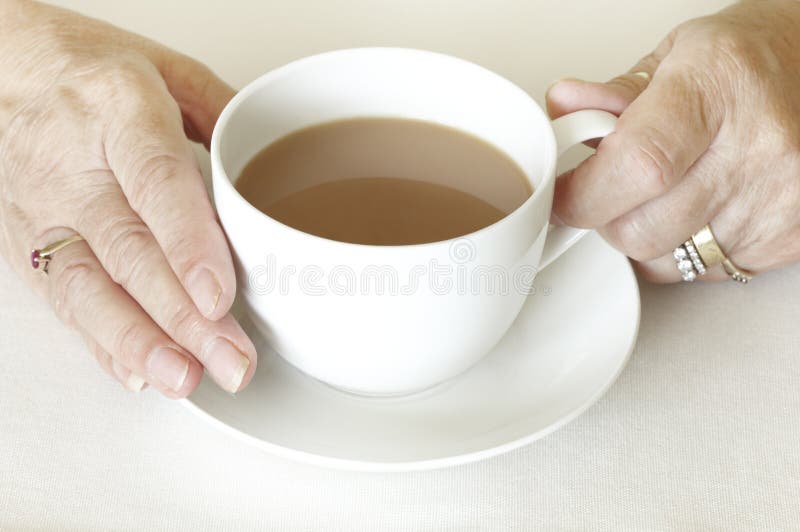 Senior womans hands holding a cup of tea on white table cloth. Senior womans hands holding a cup of tea on white table cloth