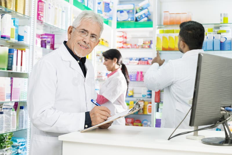 Starszy chemika Writing Na schowku Podczas gdy Coworkers Pracuje W P obraz stock Starszy chemika Writing Na schowku Podczas gdy Coworkers Pracuje W P obraz stock