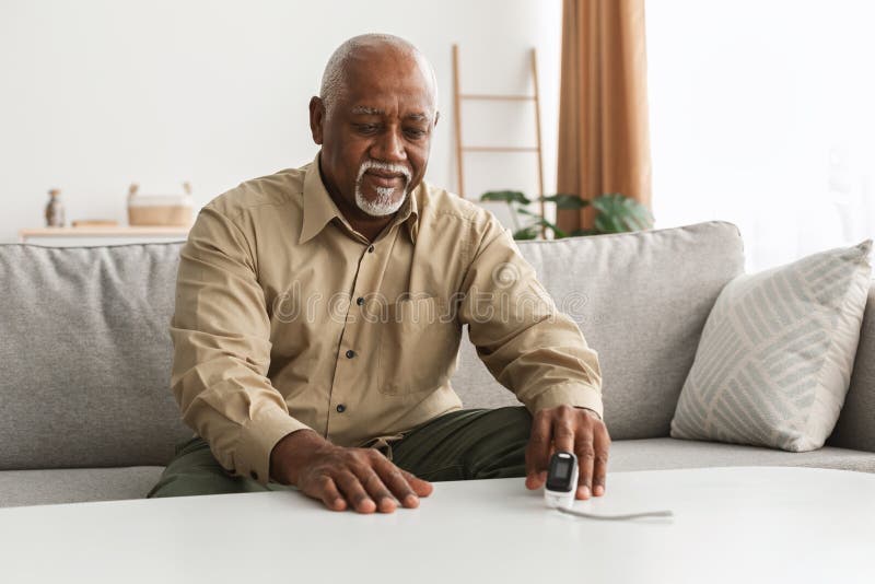 Starszy czarny mężczyzna mierzący nasycenie tlenem przy użyciu utleniacza impulsowego w pomieszczeniu