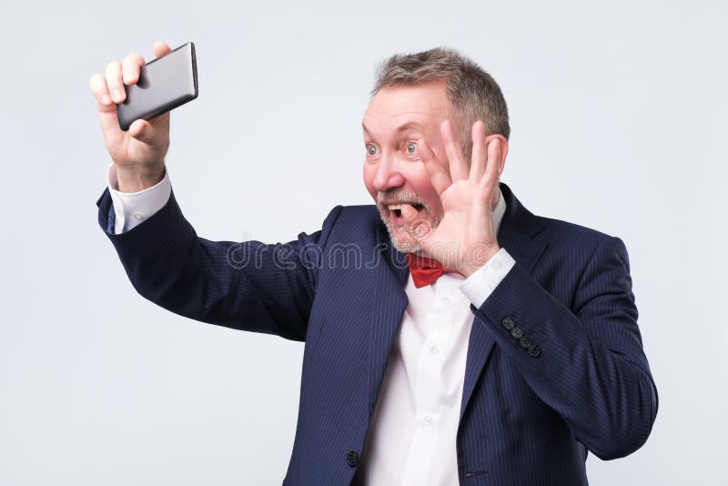 Starszy mężczyzna patrzeje ekran mądrze telefon, macha cześć mieć wideo gadkę jak obrazy stock Starszy mężczyzna patrzeje ekran mądrze telefon, macha cześć mieć wideo gadkę jak obrazy stock