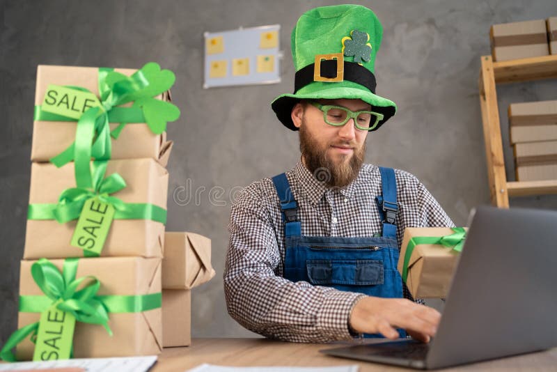 Starta en framgångsrik småföretagsägare i leprechaun-hatt som arbetar hemifrån med bärbara datorer och köp online royaltyfria bilder