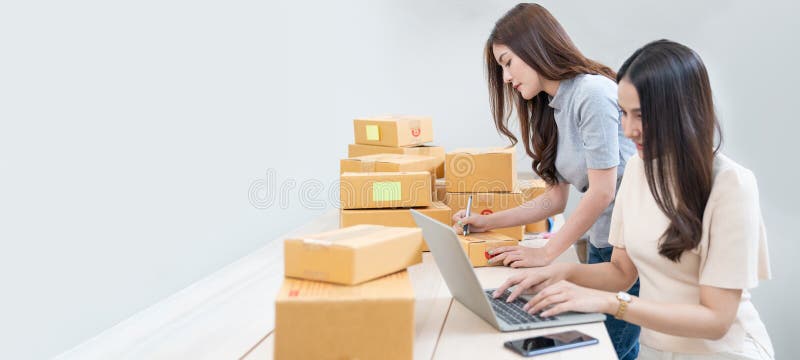 Startup small business owner working with computer at workplace. Freelance two woman seller check product order. Packing goods for