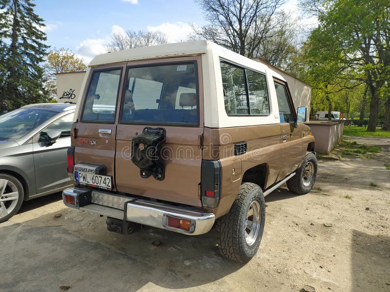 Old brown white offroad four wheel drive classic veteran vintage car Toyota Landcruiser Turbo LX 4WD J70 2-door hardtop parked in Gdansk Wrzeszcz in northern Poland. Right side and rear part view. Fibre reinforced plastic top. Model manufactured from 1984. Modern electric streetcars in the background. April 15th, 2024. Old brown white offroad four wheel drive classic veteran vintage car Toyota Landcruiser Turbo LX 4WD J70 2-door hardtop parked in Gdansk Wrzeszcz in northern Poland. Right side and rear part view. Fibre reinforced plastic top. Model manufactured from 1984. Modern electric streetcars in the background. April 15th, 2024.