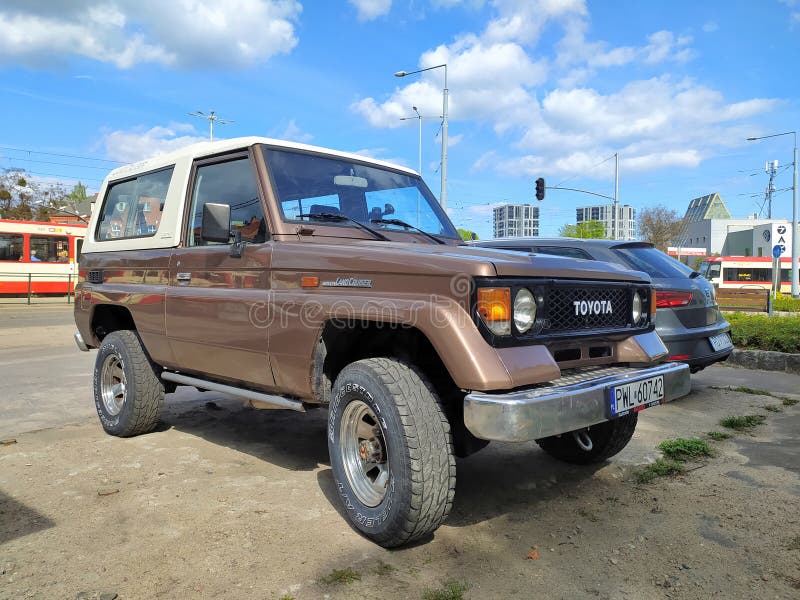 Old big brown white offroad four wheel drive car Toyota Landcruiser Turbo LX 4WD J70 2-door hardtop parked in Gdansk Wrzeszcz in northern Poland. Right side and front view with grille and chromed bumper. Fibre reinforced plastic top. Model manufactured from 1984. Modern electric streetcars in the background. April 15th, 2024. Old big brown white offroad four wheel drive car Toyota Landcruiser Turbo LX 4WD J70 2-door hardtop parked in Gdansk Wrzeszcz in northern Poland. Right side and front view with grille and chromed bumper. Fibre reinforced plastic top. Model manufactured from 1984. Modern electric streetcars in the background. April 15th, 2024.