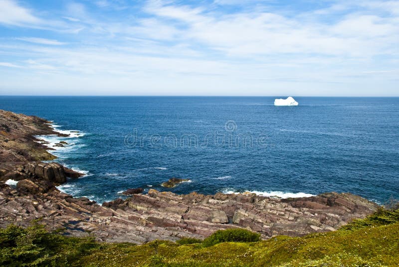 Newfoundland Iceberg on Calm North Atlantic with Horizon in Background and Heavily Layered Shoreline Geology in Foreground. Newfoundland Iceberg on Calm North Atlantic with Horizon in Background and Heavily Layered Shoreline Geology in Foreground.