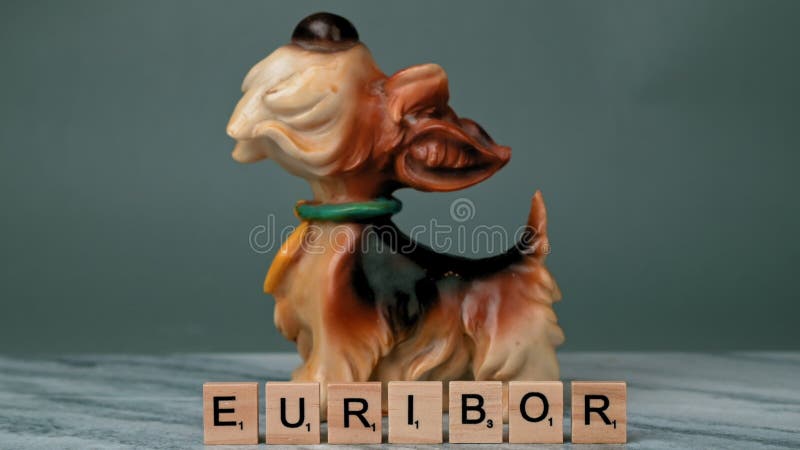 Static Shot of Word EURIBOR Is Written In Wooden Letters. Behind Piggy Bank in Form of Dog and Woman\'s Hand