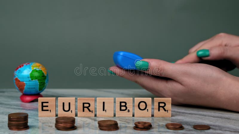 Static Shot of Word EURIBOR Is Written In Wooden Letters. In Foreground, Piles of Euro Cents. Behind Woman