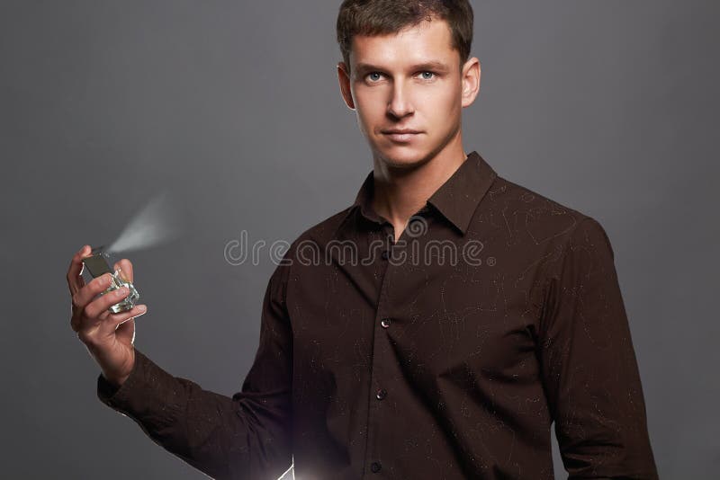 Stattlicher junger Mann, der Duftstoff verwendet Parfümflasche und Sprühduft stockfotografie Stattlicher junger Mann, der Duftstoff verwendet Parfümflasche und Sprühduft stockfotografie