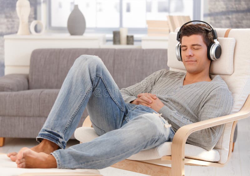 Handsome guy enjoying music on headphones, sitting in armchair with eyes closed, smiling. Handsome guy enjoying music on headphones, sitting in armchair with eyes closed, smiling.