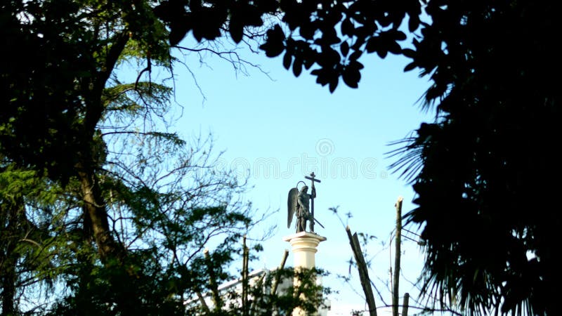 Statue brouill?e de silhouette d'un ange avec une ?p?e contre le ciel bleu dans le cadre du feuillage photos libres de droits Statue brouill?e de silhouette d'un ange avec une ?p?e contre le ciel bleu dans le cadre du feuillage photos libres de droits