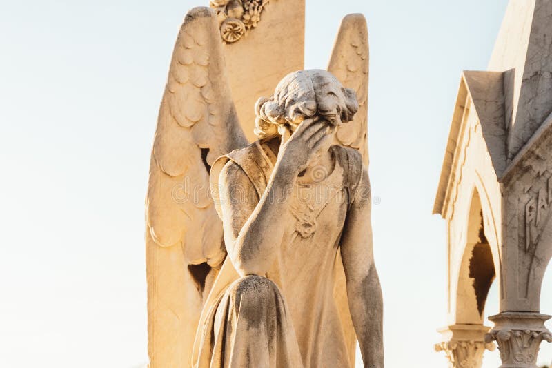 Statue of angel with wings against light sky at cemetery. Closing stoned angel praying in an old cemetery. Graveyard old crying angel sculpture on funeral. Death, loss, condolence concept. empty space background. Statue of angel with wings against light sky at cemetery. Closing stoned angel praying in an old cemetery. Graveyard old crying angel sculpture on funeral. Death, loss, condolence concept. empty space background