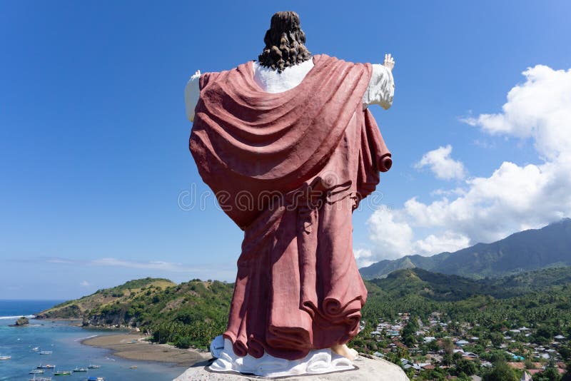 A statue of Jesus Christ laid on a hill, facing the ocean and a village in Flores, East Nusa Tenggara, Indonesia. Aerial, landmark, america, architecture, clouds, famous, travel, beautiful, view, city, bay, coast, high, water, sightseeing, praia, copy-space, south, beach, sculpture, urban, redeemer, helicopter, vacation, buildings, stone, christian, landscape, sky, tourism, sea, monument, touristic, holy, scenic, scene, boat, country, asia, blessed, forest