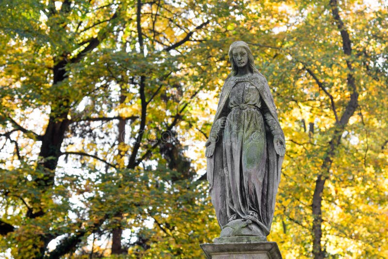 Statue of Mary Mother of God, at autumn tree backgroung, copy space. Religious symbol.