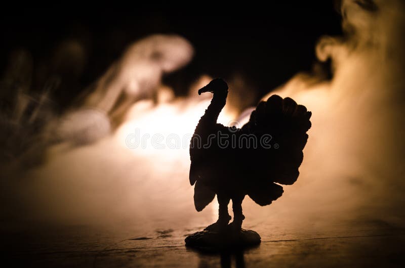 Statue of Turkey Tom strutting his stuff with red wattles and blue/white head on a smoke toned dark background. With empty space. Festive, fleshy.