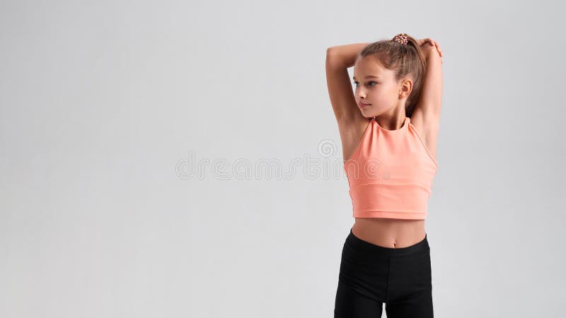 Stay healthy. Flexible cute little girl child looking aside while stretching her body isolated on a grey background