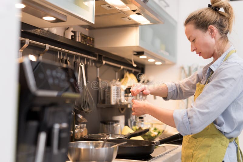 Stay at home housewife woman cooking in kitchen, salting dish in a saucepan, preparing food for family dinner.