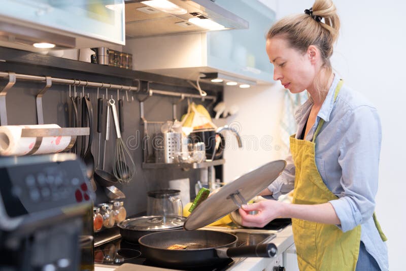 Stay at home housewife woman cooking in kitchen, stir frying dish in a saucepan, preparing food for family dinner.