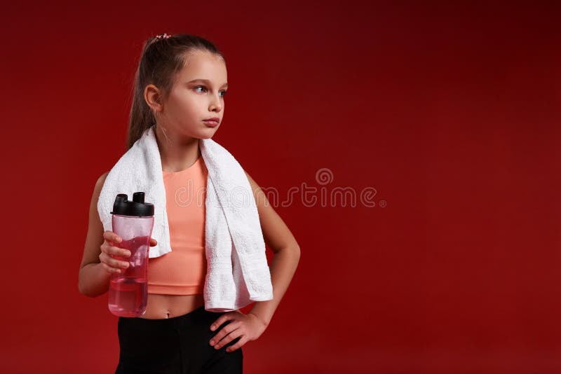 Stay hydrated. A cute girl engaged in sport, looking aside while standing with towel and bottle of water. Isolated on