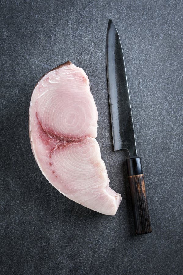 Raw and fresh sword fish steak offered with a Japanese Gyuto knife as top view on a gray design board. Raw and fresh sword fish steak offered with a Japanese Gyuto knife as top view on a gray design board