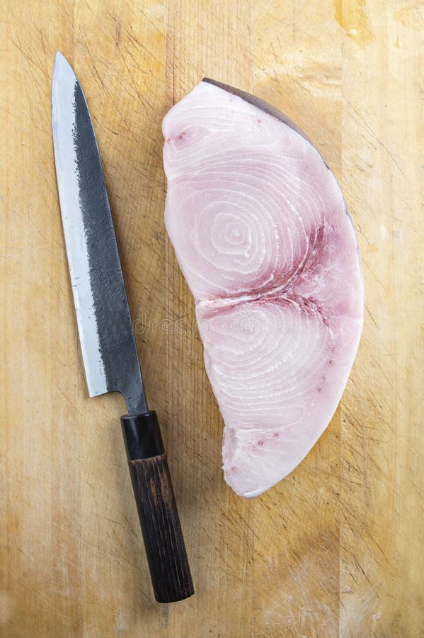 Raw and fresh sword fish steak offered with a Japanese Gyuto knife as top view on a wooden board. Raw and fresh sword fish steak offered with a Japanese Gyuto knife as top view on a wooden board