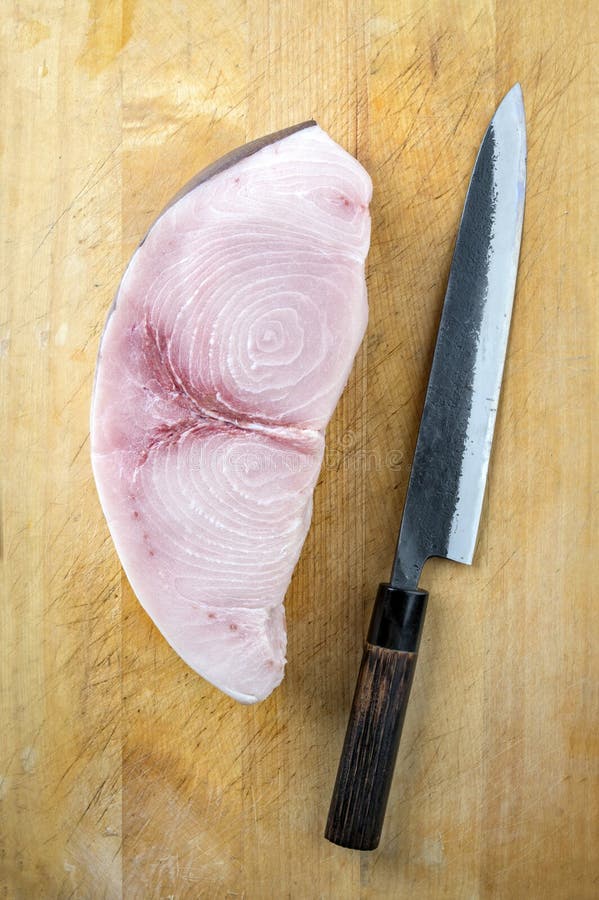 Raw and fresh sword fish steak offered with a Japanese Gyuto knife as top view on a wooden board. Raw and fresh sword fish steak offered with a Japanese Gyuto knife as top view on a wooden board