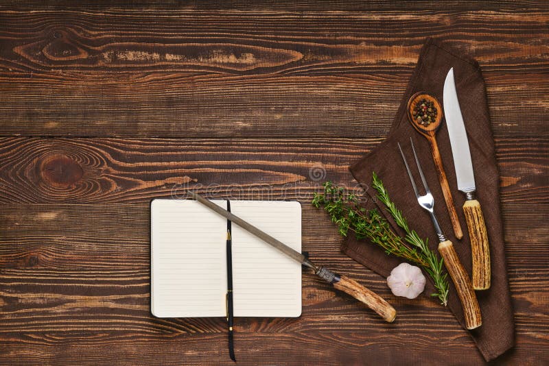 Steak fork, knife and sharpener on wooden table next to notebook stock photo