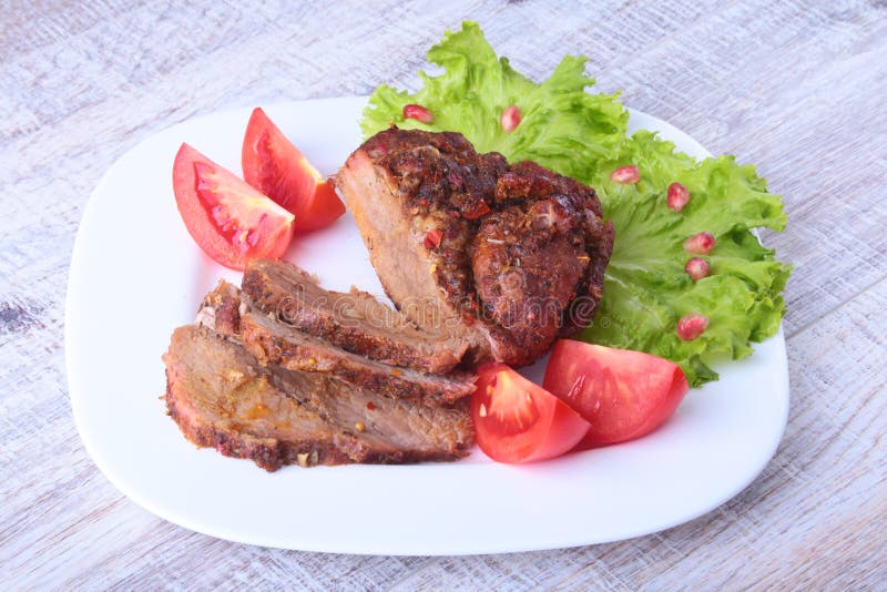 Steak of grilled meat with tomato, lettuce and beans pomegranate on white plate.