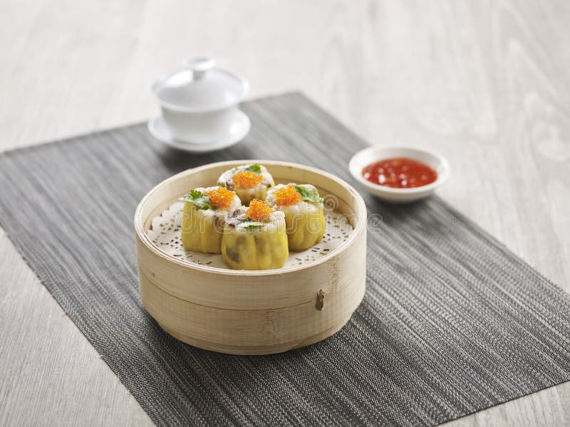 Steamed Pork Dumpling Siew Mai served in a wooden bowl with chopsticks isolated on mat side view on grey marble background