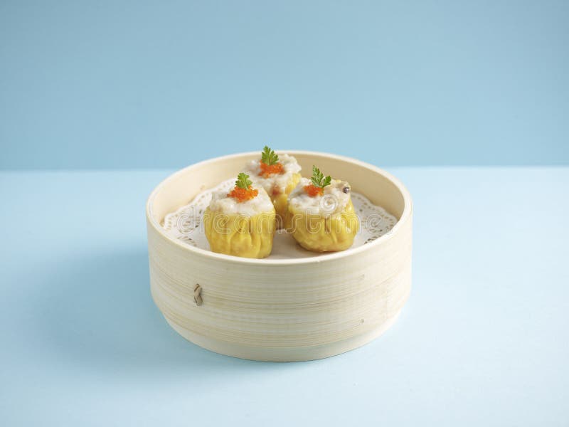 Steamed Pork Dumpling Siew Mai served in a wooden bowl with chopsticks isolated on mat side view on grey marble background.