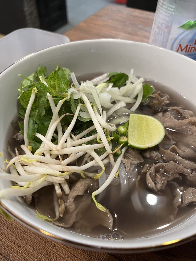 Steaming bowl of Vietnamese Pho, a beloved traditional noodle soup. The dish includes a flavorful, clear broth, tender slices of beef, and silky rice noodles. Garnished with bean sprouts, fresh herbs like mint and cilantro, and thinly sliced onions, it's a perfect harmony of freshness and comfort. Mint vietnamese stock images, royalty-free photos and pictures