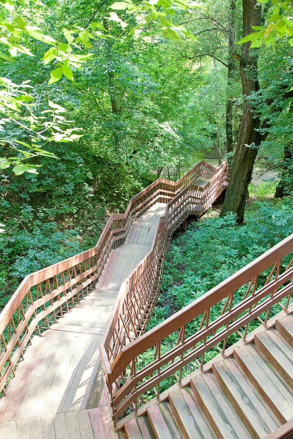 A winding steep staircase with stone steps and iron rails against the  background of beautiful climbing plants Stock Photo