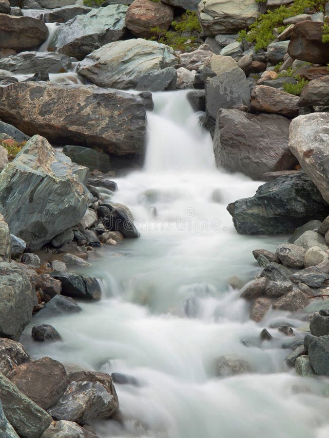 Steep stony stream bed of Alpine brook. Blurred waves of stream running over boulders and stones, high water level after rains