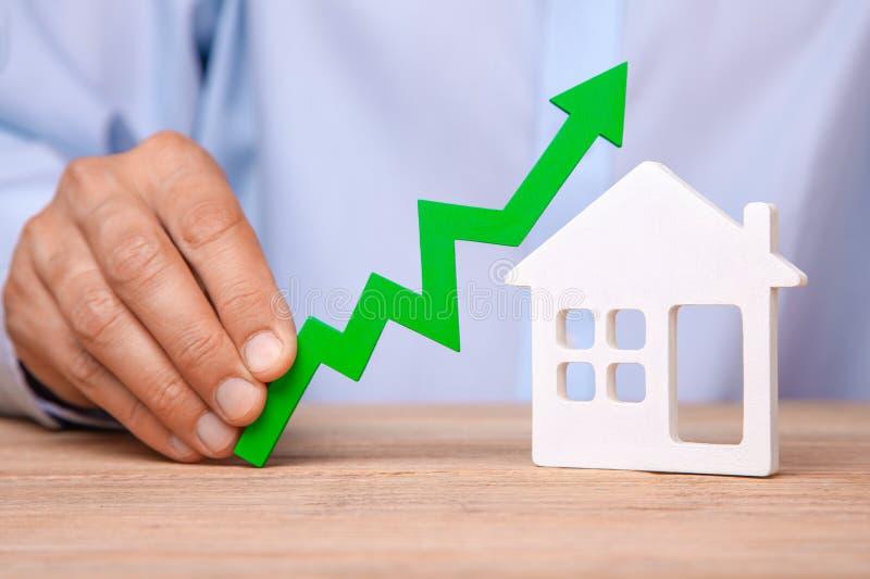 Steigende Wohnungspreise Mann hält grünen Pfeil oben in seiner Hand und in Haus