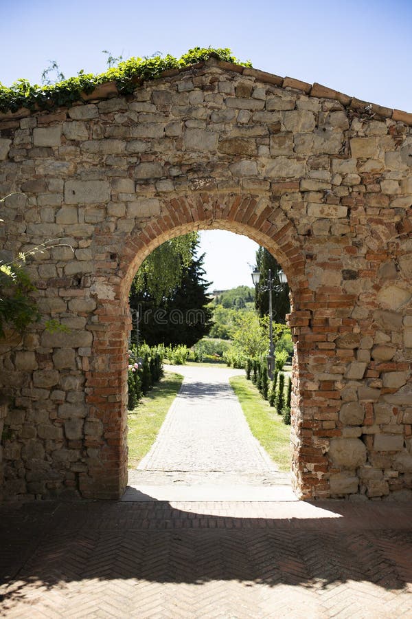 Brickstone arch and passage  in Fortunago, one of the most charming villages of Oltrepò Pavese, Lombardia countryside, Italy. Green park in the background. Vertical shot. Brickstone arch and passage  in Fortunago, one of the most charming villages of Oltrepò Pavese, Lombardia countryside, Italy. Green park in the background. Vertical shot