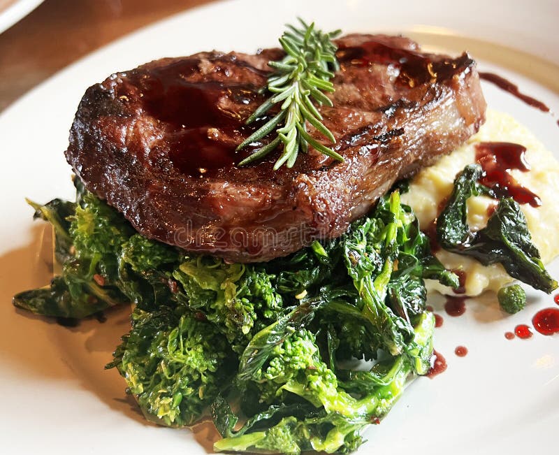 Stek na brokułach z polantem. Charbroiled flatiron sirloin steak on broccolini with polenta and red wine reduction sos top with rosemary on white plate in restauracja