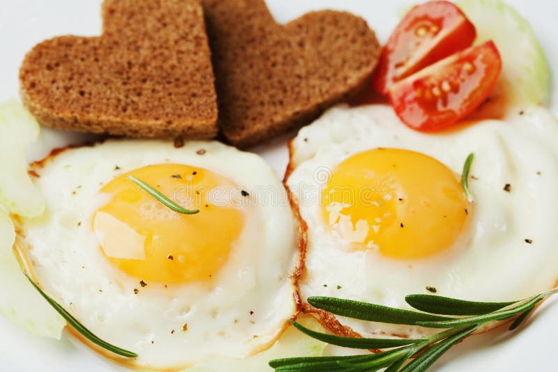 Stekte ägg med nya grönsaker och rostat bröd i form av hjärta på den vita plattan