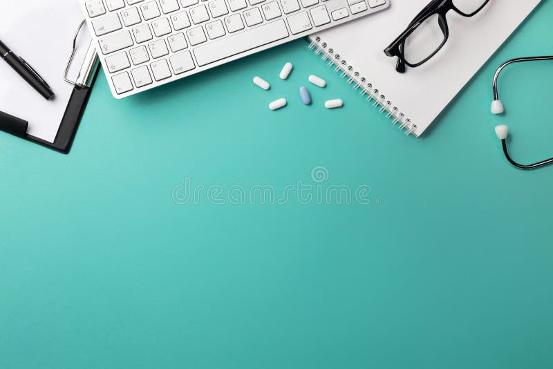 Stethoscope in doctors desk with notebook, pen, keyboard, mouse and pills