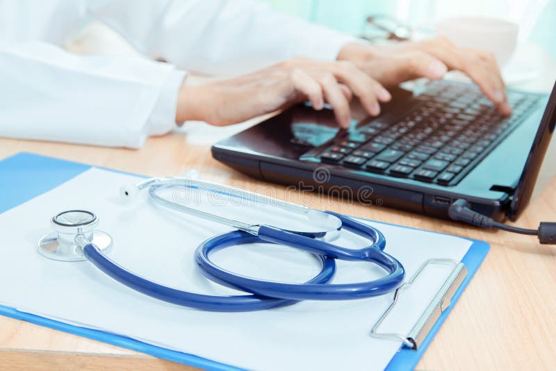 Stethoskop auf Schreibtisch mit Doktor unter Verwendung der DigitaltechnikLaptop-Computers lizenzfreies stockbild Stethoskop auf Schreibtisch mit Doktor unter Verwendung der DigitaltechnikLaptop-Computers lizenzfreies stockbild