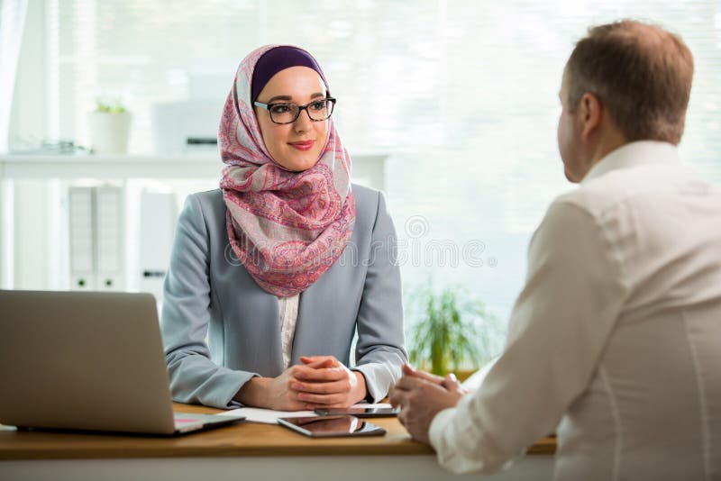Stilfull kvinna i hijab som g?r konversation p? skrivbordet med mannen