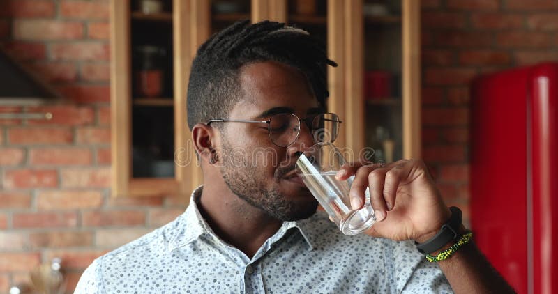 Stilig afrikansk man som står i köket och dricker fortfarande vatten lager videofilmer