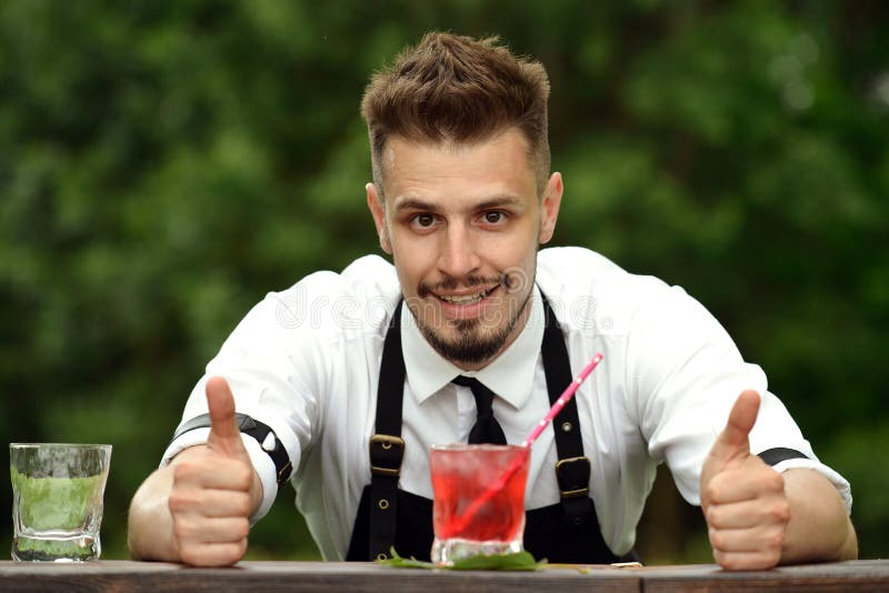 Stilig bartender som står nära stångräknare och tummar upp, selecti royaltyfri foto Stilig bartender som står nära stångräknare och tummar upp, selecti royaltyfri foto