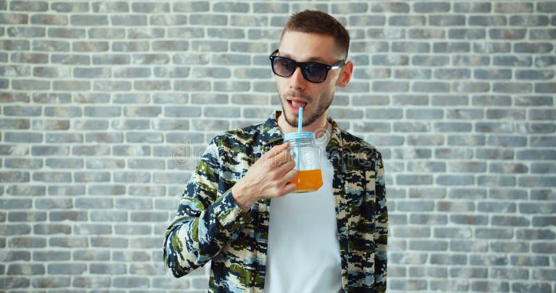 Stilig man i solglasögon som dricker orange fruktsaft som visar att le för tummar-upp stock video