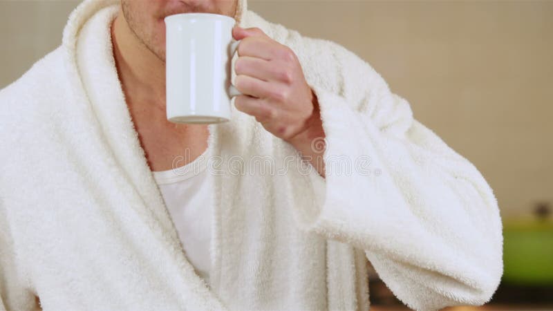 Stilig man som dricker kaffe i badämbetsdräkt lager videofilmer