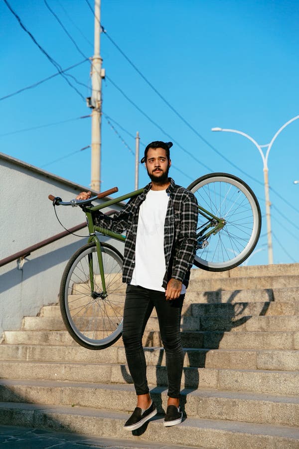 Stilig man som rymmer en cykel på hans skuldra, medan gå ner på moment arkivbilder Stilig man som rymmer en cykel på hans skuldra, medan gå ner på moment arkivbilder