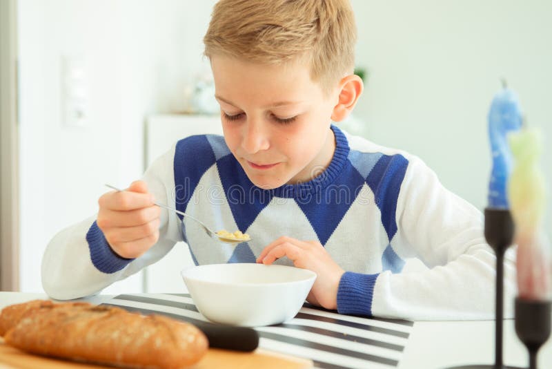 Handsome teenager eating soup and whole grain bread in bright living room at home. Handsome teenager eating soup and whole grain bread in bright living room at home