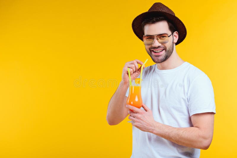 stilig ung man i hatt och solglasögon som dricker sommarcoctailen och ler på kameran royaltyfri bild stilig ung man i hatt och solglasögon som dricker sommarcoctailen och ler på kameran royaltyfri bild