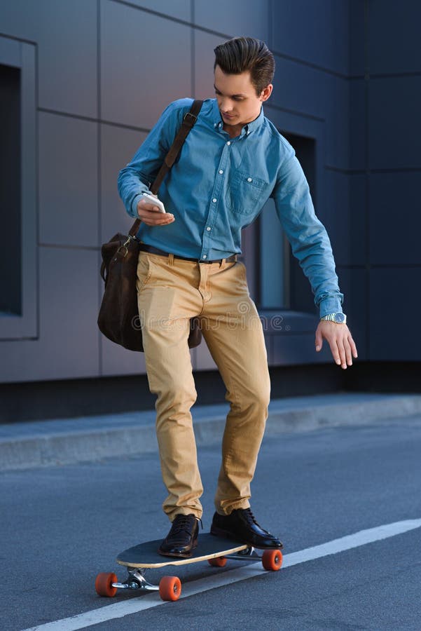 stilig ung man som använder smartphonen och rider skateboarden arkivfoton stilig ung man som använder smartphonen och rider skateboarden arkivfoton
