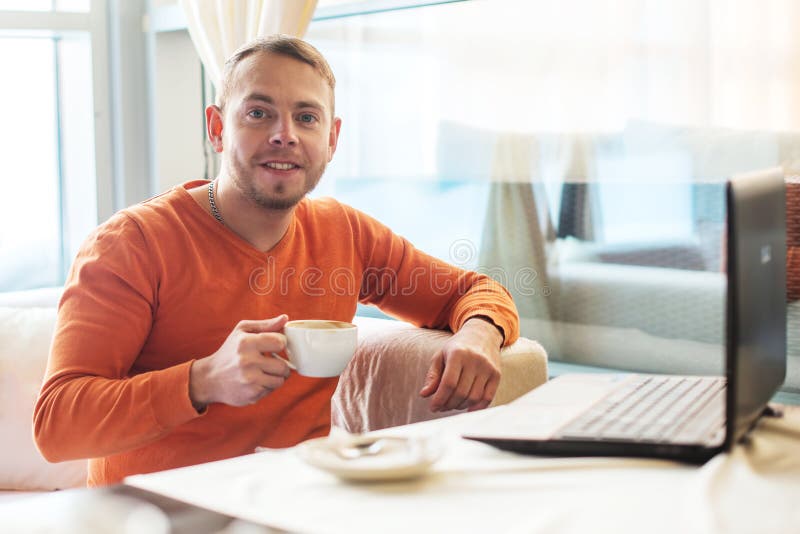 Stilig ung man som arbetar på anteckningsboken, le som ser kameran, medan tycka om kaffe i kafé royaltyfri fotografi Stilig ung man som arbetar på anteckningsboken, le som ser kameran, medan tycka om kaffe i kafé royaltyfri fotografi